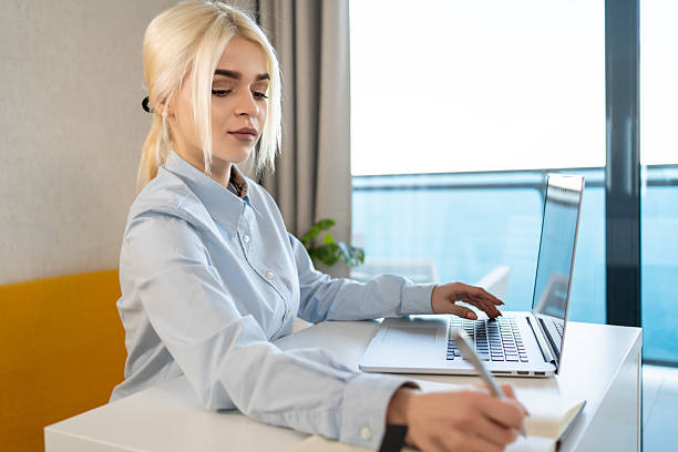 istock Businesswoman taking notes while working on laptop in home office for productivity, task planning, remote work, freelance projects, career development, digital workspace, time management 2236114055