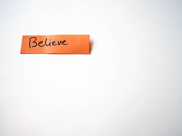 The word Believe handwritten on an orange sticky note against a white background