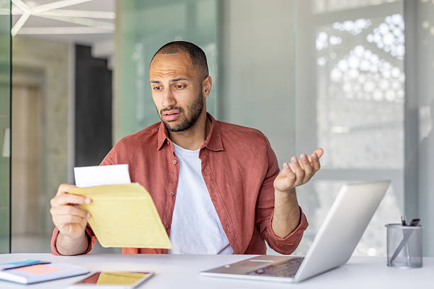 istock Confused man reviews a letter with concern in a modern office environment. 2236123366