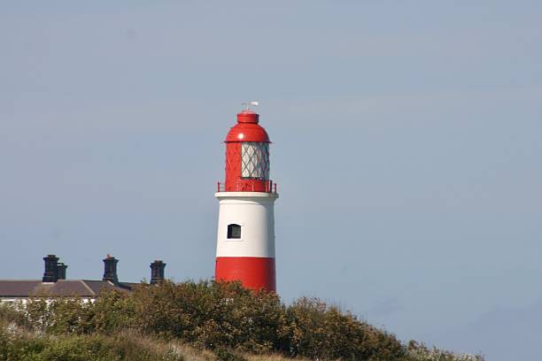 istock Bright red and white striped lighthouse stands tall under a clear blue sky, serving as a coastal beacon. Traditional structure with lantern room, perfect for maritime, travel, or coastal themes. 2236124103