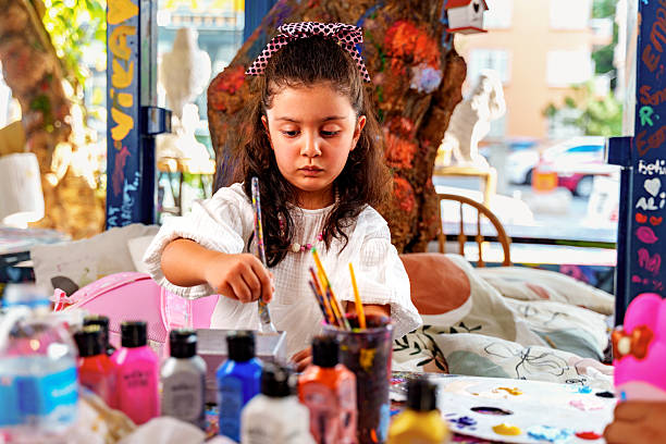 A little girl is painting  box during an art class at a colorful studio. The child focuses on carefully adding details with a brush. Concept of creativity, childhood development, art education