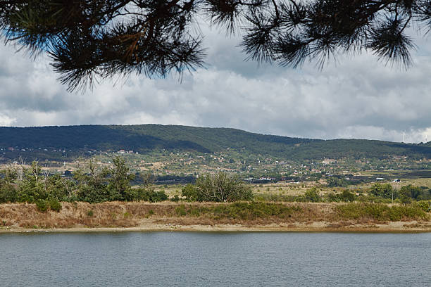 istock Scenic landscape village on a hillside featuring a tranquil lake surrounded by lush greenery and distant hills under a cloudy sky, creating a serene natural atmosphere for relaxation and reflection 2236124872