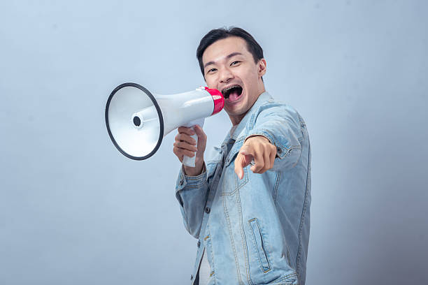 istock Asian man in denim jacket holding a megaphone while pointing forward, smiling and shouting, symbolizing leadership, communication, motivation, or public announcement 2236126778