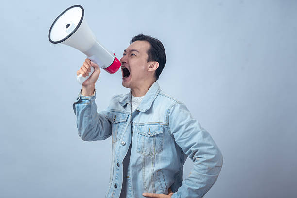 istock Asian man in denim jacket shouting through a white megaphone with an expressive face, symbolizing announcement, protest, communication, speech, or leadership 2236127877