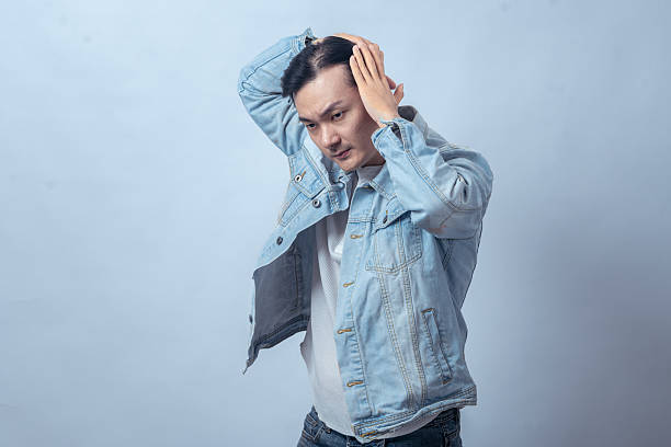 istock Asian man in denim jacket styling hair with hands against plain studio background, expressing confidence, grooming, lifestyle, and fashion concept for modern casual male portrait 2236128709