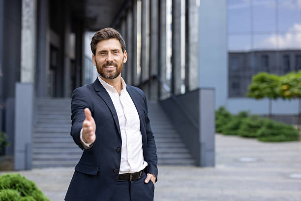 istock Confident businessman extends handshake outdoors near modern office building 2236132199