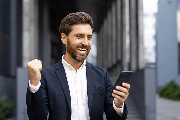 istock Delighted man holding smartphone while celebrating success outdoors in urban setting 2236132224
