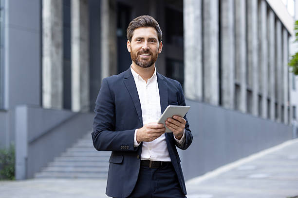 istock Smiling businessman holding a tablet outside modern building in urban setting 2236132239