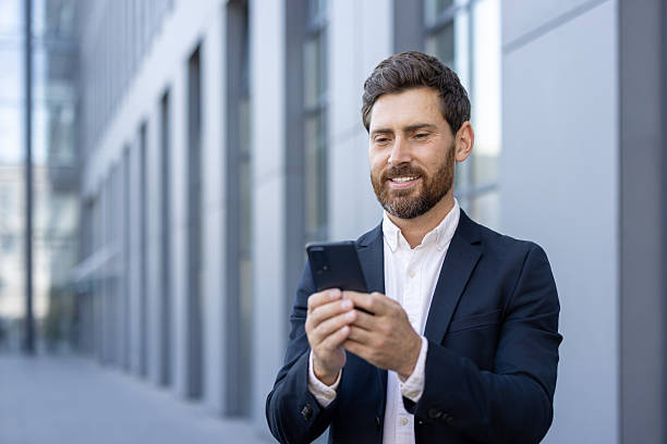 istock Smiling businessman using smartphone outside in office building surroundings 2236132264