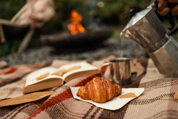 istock Camping breakfast scene with coffee, croissant, and a book by the campfire. 2236132757