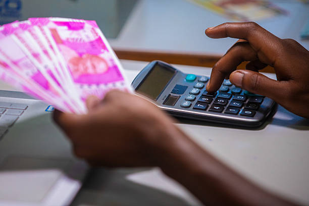 istock Dark skinned African person sitting punching pressing calculator with Indian Rupee notes on table desk 2236140966