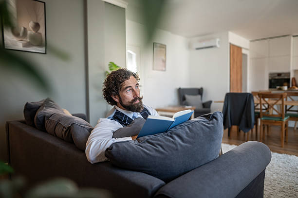 istock Man reading book on couch thinking and relaxing 2236154345
