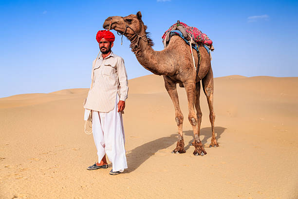 istock Indian man holding camel on sand dunes, Rajasthan, India 2236155735