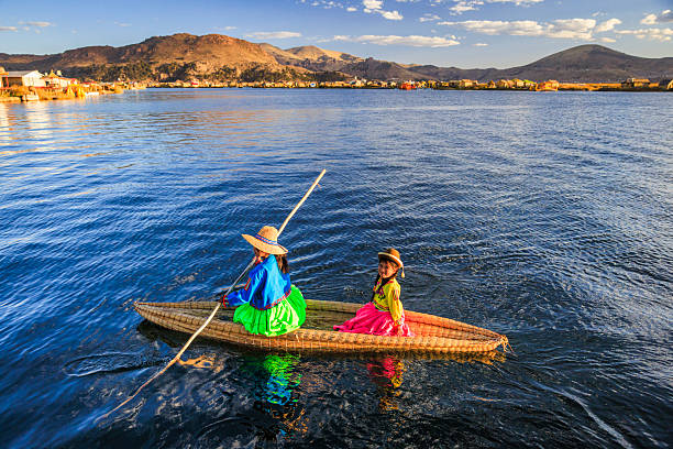 Peruvian woman sailing between Uros floating islands. Uros are a pre-Incan people that live on forty-two self-fashioned floating island in Lake Titicaca Puno, Peru and Bolivia. They form three main groups: Uru-Chipayas, Uru-Muratos  and the Uru-Iruitos. The latter are still located on the Bolivian side of Lake Titicaca and Desaguadero River. The Uros use bundles of dried totora reeds to make reed boats (balsas mats), and to make the islands themselves. The Uros islands at 3810 meters above sea level are just five kilometers west from Puno port.