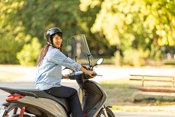 istock Young Woman Riding a Motor Scooter in a Beautiful Sunny Park Setting 2236157622