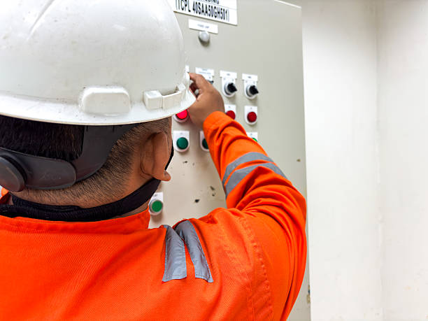 istock Engineer controlling industrial panel with safety equipment performing routine checks adjusting switches in orange protective workwear with white helmet inspecting factory controls 2236159049