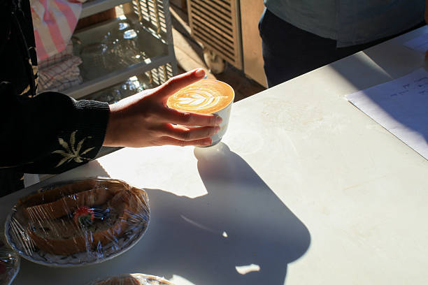 Barista making hot latte with foam milk art on counter in coffee shop under sunlight. Morning breakfast.