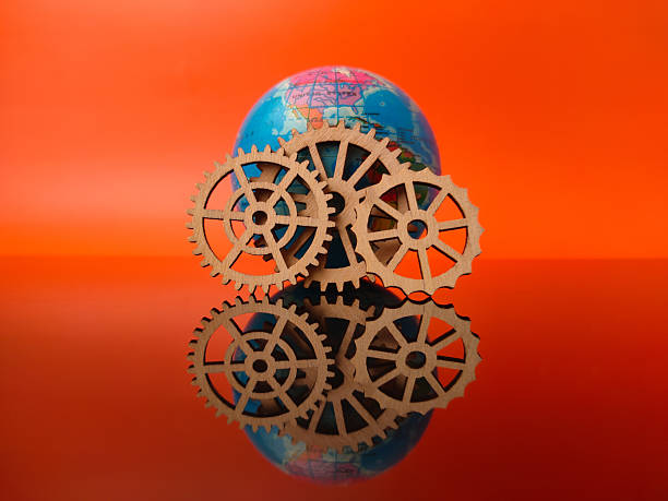 istock The globe surrounded by wooden gears, resting on a reflective surface against an orange background 2236182501