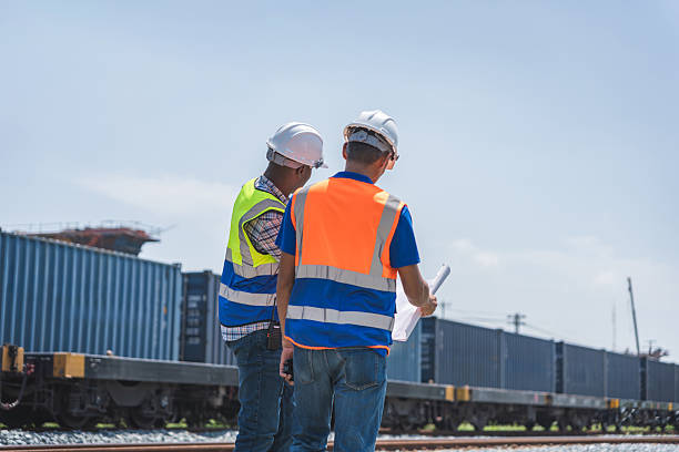 istock Construction Engineers Discussing Plans at a Rail Yard, Rear View of Workers in Hard Hats Examining Blueprints, Supervisors Inspecting a Railway Construction Site 2236186500
