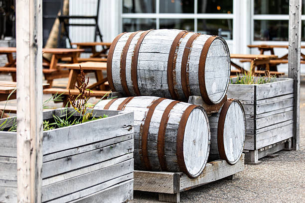 A collection of aged wooden barrels sitting in an outdoor seating area, surrounded by rustic planters filled with greenery, evoking a natural and classic ambiance at an open-air cafe or garden.