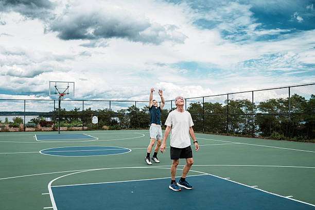 A man takes a jump shot as his senior friend looks up during a friendly one-on-one basketball game on an outdoor court in Portland, Maine.