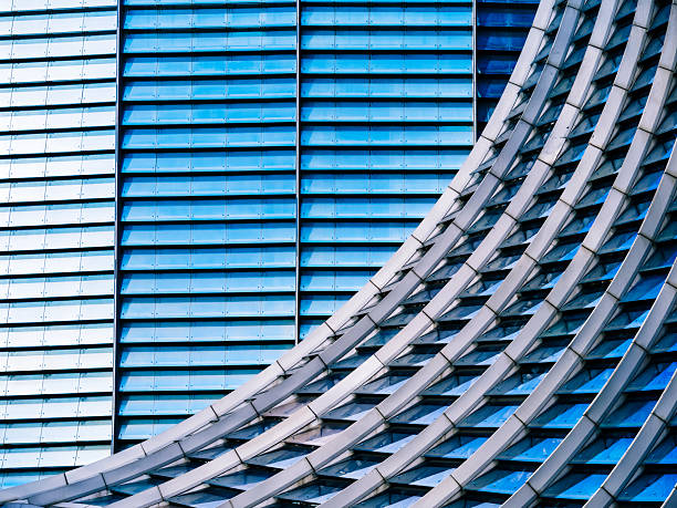 A close-up of a modern building facade showcasing its unique wavy glass design. The intricate, undulating pattern of the windows reflects light and shadows, giving the structure a dynamic and architectural elegance.