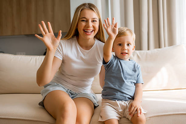 istock Happy mother and child waving while sitting together on a comfortable sofa 2236200044
