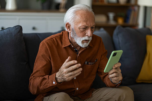 istock Shocked senior man using phone while sitting on sofa at home. 2236200287