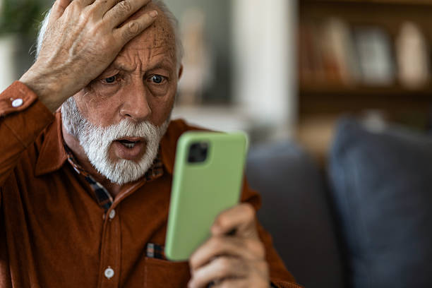 istock Shocked senior man using phone while sitting on sofa at home. 2236200306