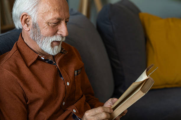 istock Senior man reading a book while sitting on sofa at home. 2236200372