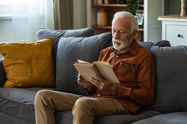 istock Senior man reading a book while sitting on sofa at home. 2236200390