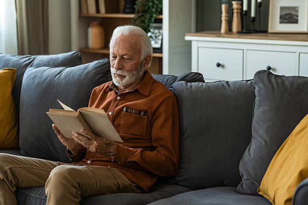 istock Senior man reading a book while sitting on sofa at home. 2236200458