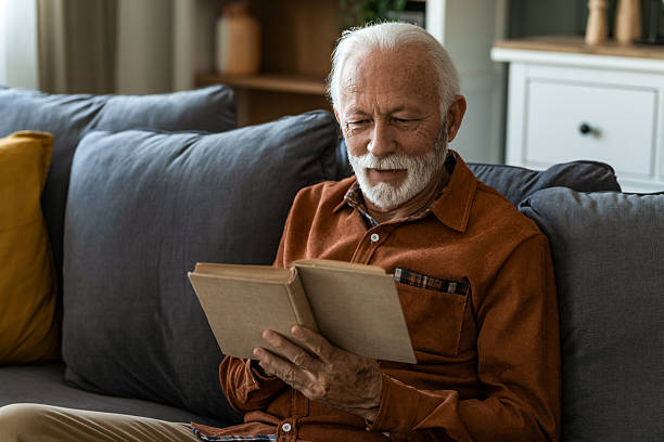 istock Senior man reading a book while sitting on sofa at home. 2236200476