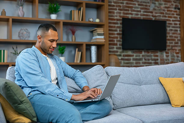 istock Relaxed man using laptop sitting on gray sofa at modern room 2236200620