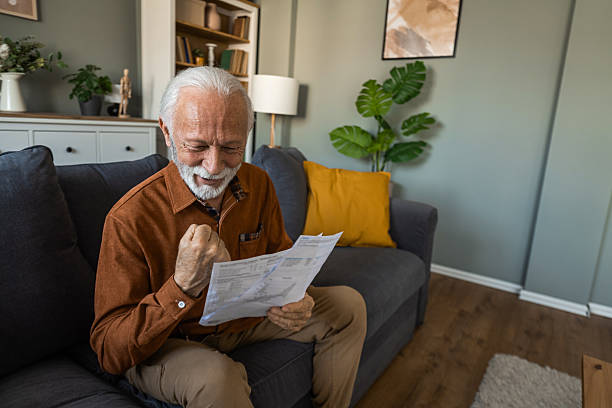 istock Cheerful senior man reading new retirement plan while sitting on sofa at home. 2236200739