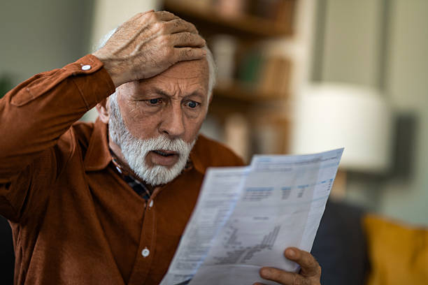 istock Shocked senior man reading new retirement plan paperwork while sitting on sofa at home. 2236200887
