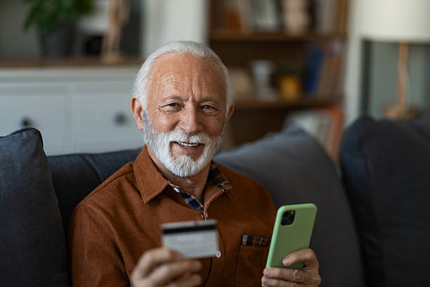 istock Senior man using phone and credit card while sitting on sofa at home. 2236201090