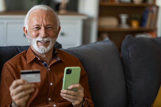 istock Senior man using phone and credit card while sitting on sofa at home. 2236201108