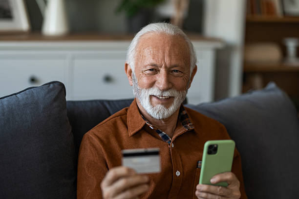 istock Senior man using cellphone and credit card while sitting on sofa at home. 2236201122
