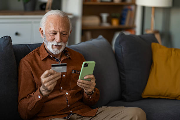 istock Happy senior man using phone and credit card while sitting on sofa at home. 2236201126