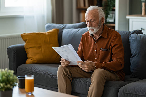 istock Serious senior man reading new retirement plan paperwork while sitting on sofa at home. 2236201236
