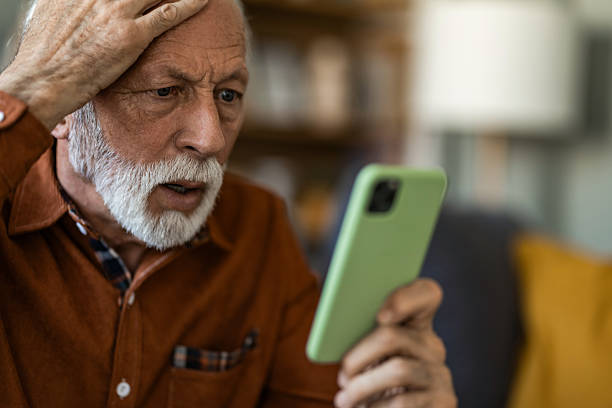 istock Shocked senior man using phone while sitting on sofa at home. 2236201268