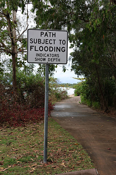 istock Path Subject To Flooding sign attached to a metal pole next to a concrete path with trees 2236205979