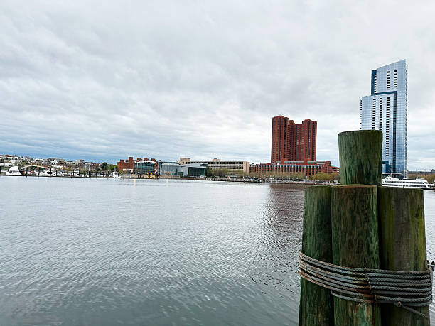 Baltimore, Maryland, USA - April 10, 2025: Urban waterfront featuring buildings, dock posts, and overcast sky, showcasing Baltimore, USA scenery