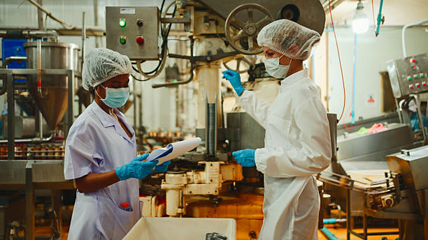 istock Two workers in protective clothing, hairnets, gloves, and boots shake hands inside a food processing facility, standing near an automated canning production line. 2236209596