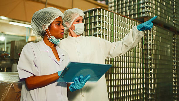 istock Two workers in protective clothing, hairnets, gloves, and boots shake hands inside a food processing facility, standing near an automated canning production line. 2236209607