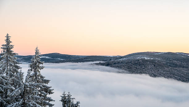 istock Winter inversion sunset with snow covered hills and forests rising above a sea of clouds, captured from above, with warm evening light painting the sky in glowing tones. 2236210708