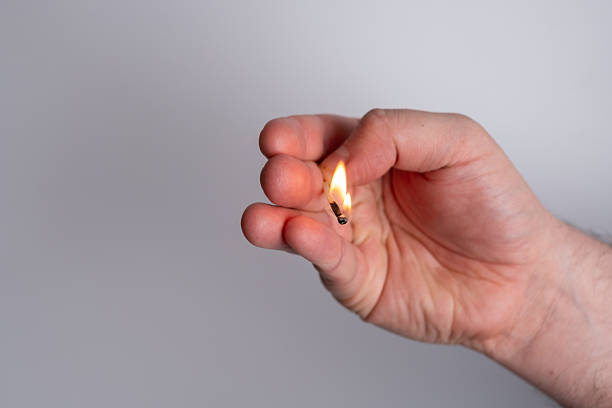 Close-up of a man's hand holding a lit match.
