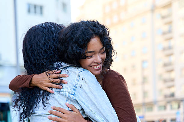 Two joyful young women embracing warmly on a bustling city street, celebrating their friendship with smiles and affection in the sunshine