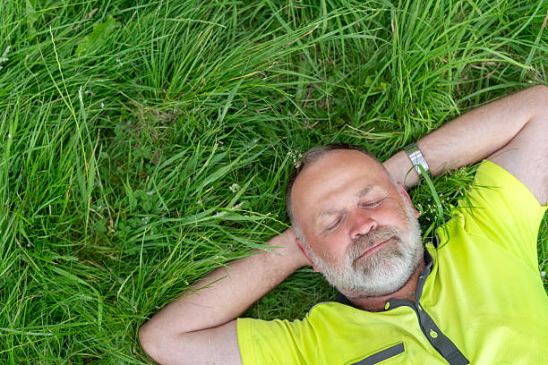 A high-angle view of a mid adult male lying down as he takes a moment to reflect and take in the beautiful surroundings whilst on a hike in Northumberland in the North East of England. He is lying with his eyes closed looking upwards.